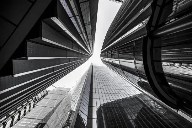 A low angle greyscale of modern skyscrapers with glass windows under sunlight